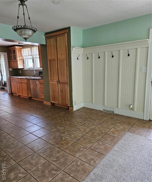 kitchen featuring a textured ceiling, stainless steel dishwasher, dark tile patterned flooring, glass insert cabinets, and brown cabinets