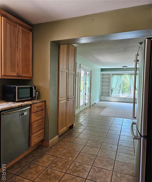 kitchen featuring stainless steel appliances, dark tile patterned floors, open floor plan, and light stone counters