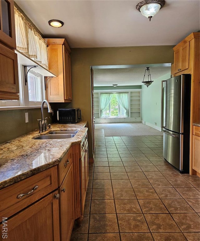 kitchen with freestanding refrigerator, a sink, dark tile patterned flooring, light stone counters, and hanging light fixtures
