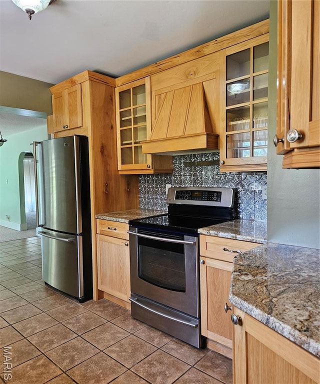 kitchen with appliances with stainless steel finishes, custom range hood, light brown cabinetry, and tile patterned flooring
