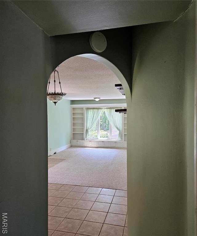 corridor featuring light carpet, a textured ceiling, arched walkways, light tile patterned flooring, and baseboards