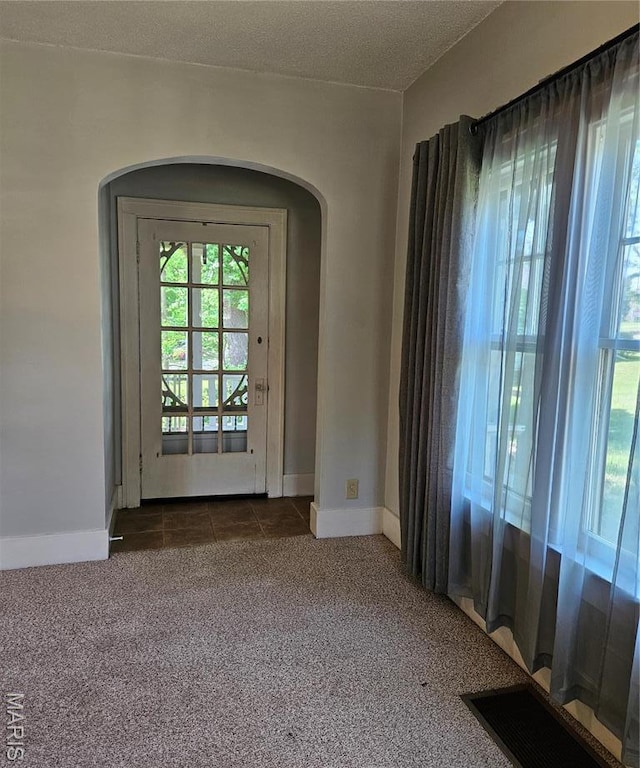 spare room with healthy amount of natural light, arched walkways, dark colored carpet, and baseboards