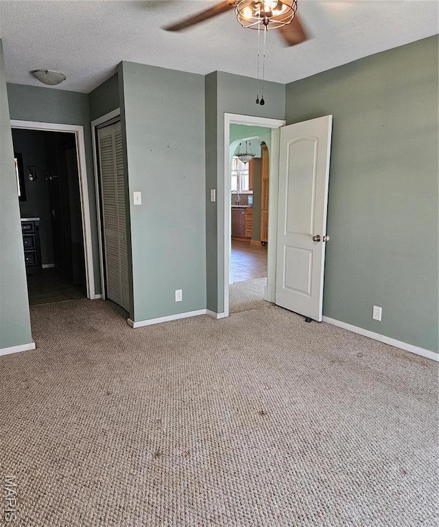 empty room featuring a ceiling fan, carpet flooring, baseboards, and arched walkways