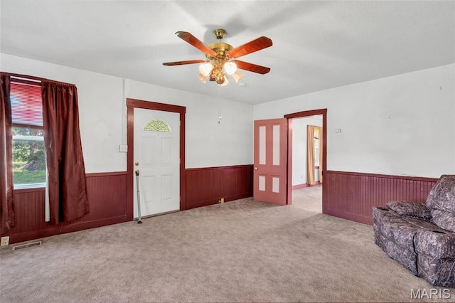 living room with wainscoting, ceiling fan, carpet, and wood walls