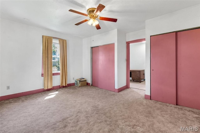 unfurnished bedroom featuring multiple closets, carpet, baseboards, and a ceiling fan