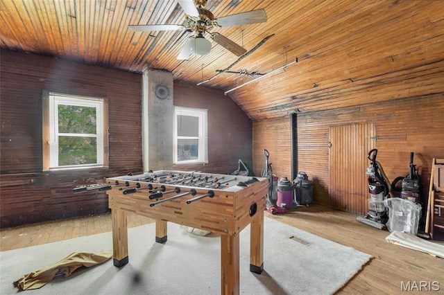 rec room with wood finished floors, wooden walls, wood ceiling, a ceiling fan, and a wood stove