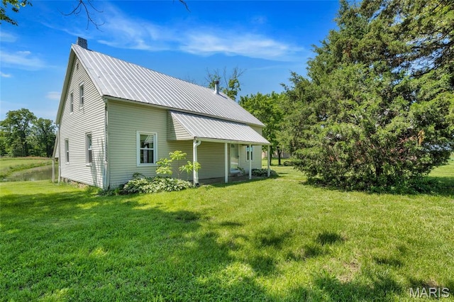 rear view of property featuring a chimney, a lawn, and metal roof