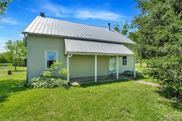 rear view of house featuring metal roof, a lawn, a standing seam roof, and a chimney