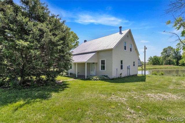 view of property exterior featuring a lawn, metal roof, a water view, and a chimney