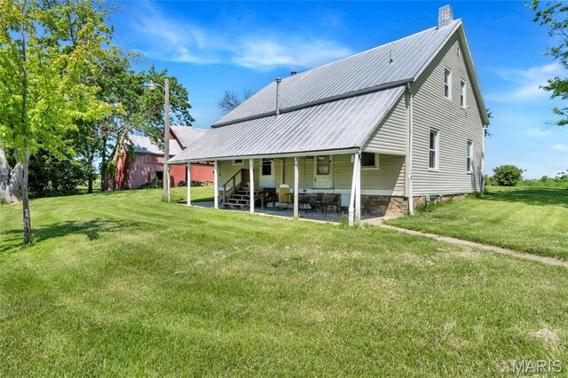 back of property with a yard, metal roof, a chimney, and a patio area