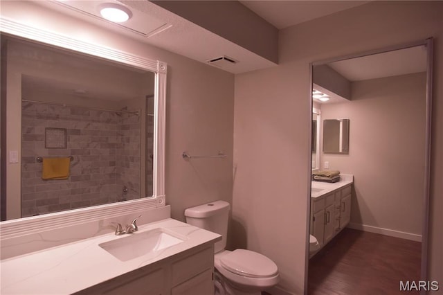 bathroom featuring toilet, vanity, a shower, wood finished floors, and baseboards