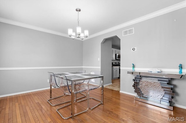 dining room with a chandelier, wood-type flooring, ornamental molding, baseboards, and arched walkways