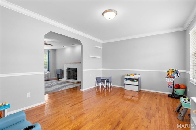 playroom featuring wood finished floors, ornamental molding, a fireplace, and baseboards