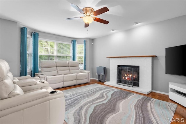 living area with a ceiling fan, wood finished floors, a brick fireplace, and baseboards