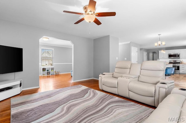 living room featuring arched walkways, light wood-style flooring, a ceiling fan, baseboards, and a chandelier