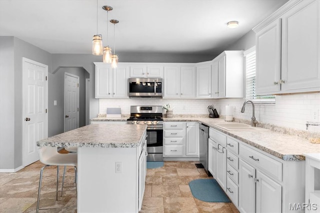 kitchen with stainless steel appliances, a sink, light stone finish floors, white cabinets, and tasteful backsplash