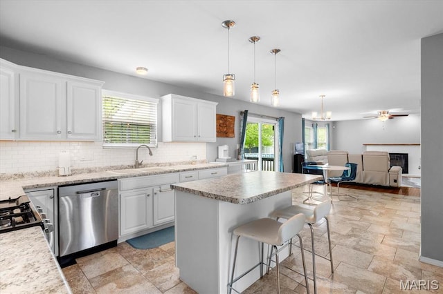 kitchen with stainless steel dishwasher, stone tile floors, tasteful backsplash, a sink, and white cabinets