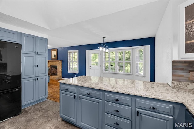 kitchen featuring freestanding refrigerator, a peninsula, a chandelier, a fireplace, and decorative light fixtures