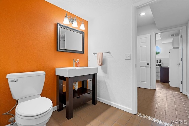half bath featuring tile patterned flooring, toilet, baseboards, and a textured wall