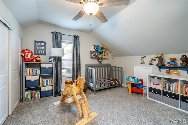 bedroom with vaulted ceiling, carpet floors, a crib, a closet, and a ceiling fan