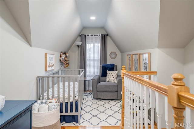 bedroom featuring lofted ceiling, a crib, and wood finished floors