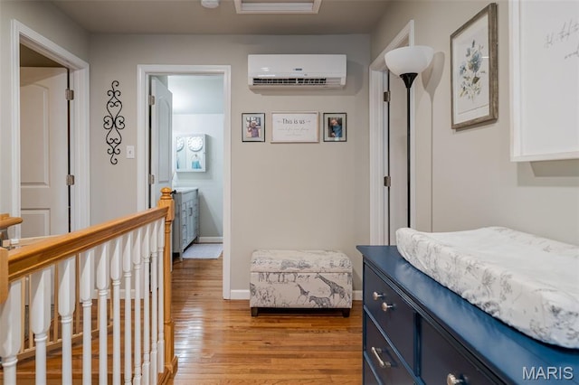 hall with a wall unit AC, light wood-style floors, baseboards, and an upstairs landing