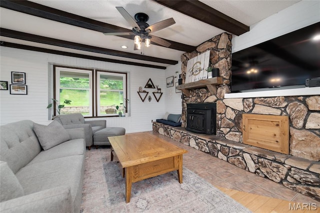 living area with a ceiling fan, beam ceiling, and a wood stove