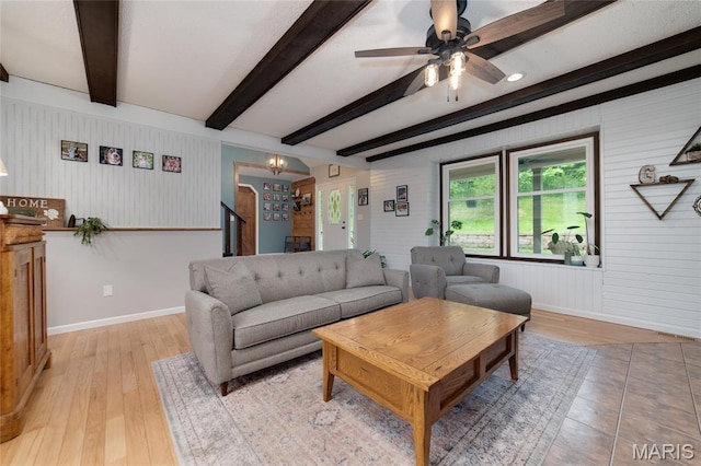 living room featuring beam ceiling, wood walls, a chandelier, light wood-type flooring, and baseboards