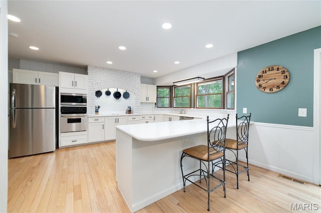 kitchen with stainless steel appliances, light wood finished floors, a kitchen breakfast bar, light countertops, and white cabinets