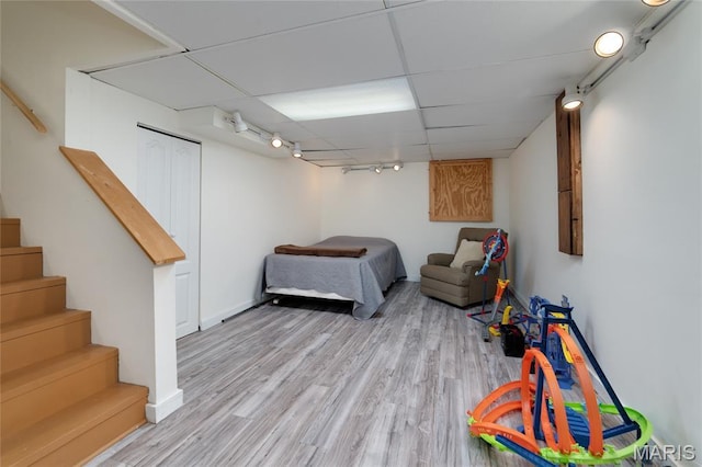 bedroom with rail lighting, light wood finished floors, a paneled ceiling, and baseboards