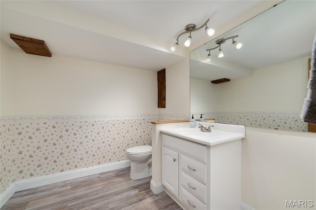 bathroom with toilet, vanity, baseboards, wood finished floors, and wallpapered walls