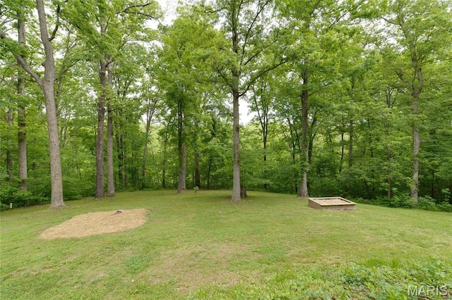 view of green lawn with a forest view