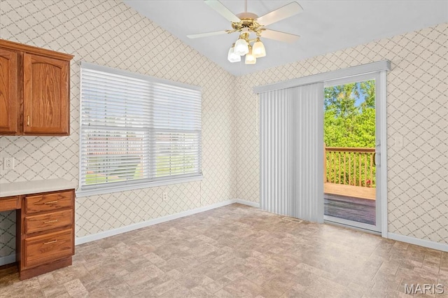 unfurnished dining area with wallpapered walls, healthy amount of natural light, ceiling fan, baseboards, and vaulted ceiling