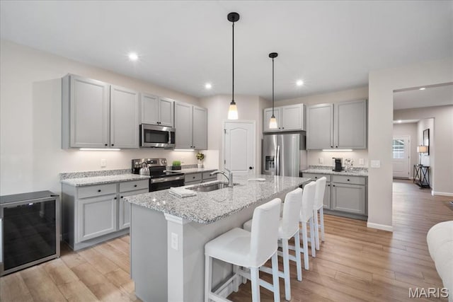 719 Myatt Dr, Wentzville, MO 63385 - kitchen with appliances with stainless steel finishes, gray cabinetry, a kitchen breakfast bar, light wood-style flooring, and light stone counters