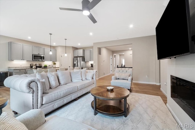 719 Myatt Dr, Wentzville, MO 63385 - living area featuring ceiling fan, light wood-type flooring, a glass covered fireplace, and recessed lighting