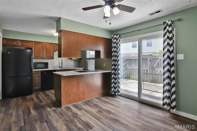 kitchen with black appliances, a peninsula, light countertops, decorative backsplash, and dark wood-style floors