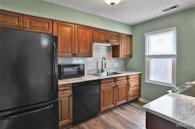 kitchen with black appliances, a sink, wood finished floors, tasteful backsplash, and a textured ceiling