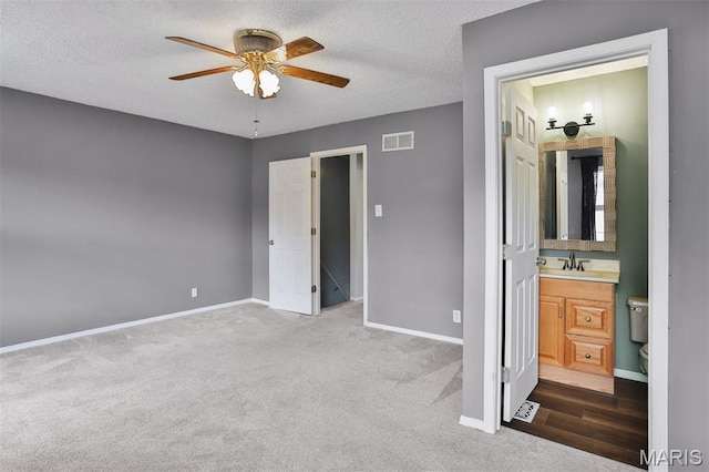 unfurnished bedroom featuring a sink, carpet, baseboards, connected bathroom, and a textured ceiling