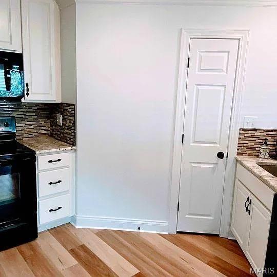 kitchen featuring black appliances, light wood finished floors, tasteful backsplash, white cabinetry, and light stone counters