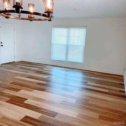 empty room featuring a chandelier, wood finished floors, and crown molding