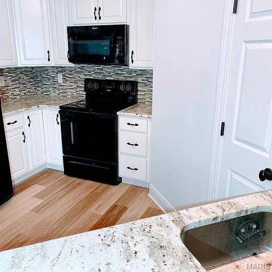 kitchen with black appliances, white cabinetry, decorative backsplash, light wood-style floors, and light stone countertops