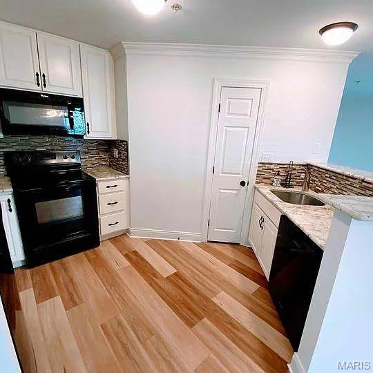 kitchen with black appliances, a sink, tasteful backsplash, white cabinetry, and light wood-style floors