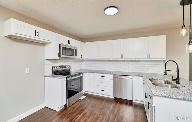 kitchen with stainless steel appliances, a sink, light stone countertops, dark wood-style flooring, and a peninsula
