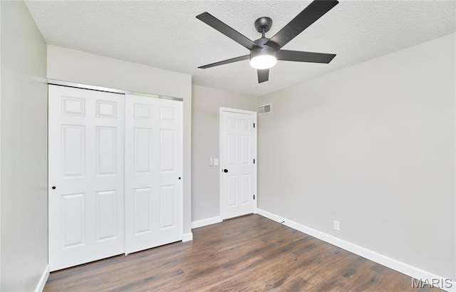 unfurnished bedroom featuring dark wood finished floors, a textured ceiling, baseboards, a closet, and a ceiling fan