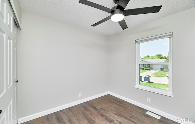 empty room with dark wood-style flooring, plenty of natural light, baseboards, a ceiling fan, and a textured ceiling