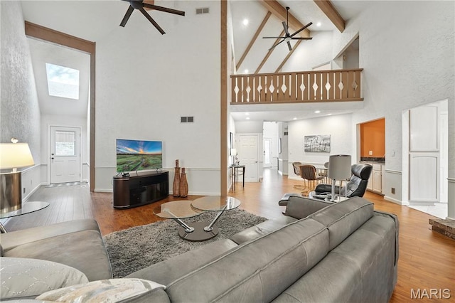 living room featuring high vaulted ceiling, a ceiling fan, light wood-type flooring, beamed ceiling, and baseboards