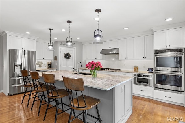 kitchen with stainless steel appliances, a sink, under cabinet range hood, white cabinetry, and recessed lighting