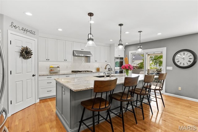 kitchen with under cabinet range hood, stainless steel appliances, a sink, light wood-style flooring, and recessed lighting
