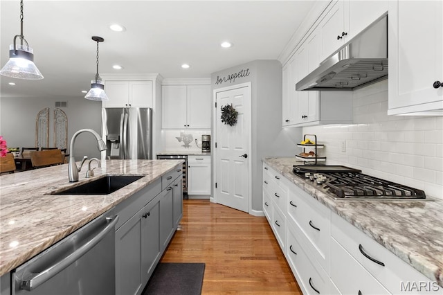 kitchen featuring appliances with stainless steel finishes, a sink, under cabinet range hood, hanging light fixtures, and backsplash