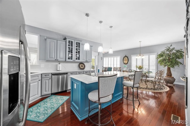 kitchen with stainless steel appliances, glass insert cabinets, a kitchen island, light countertops, and a kitchen bar